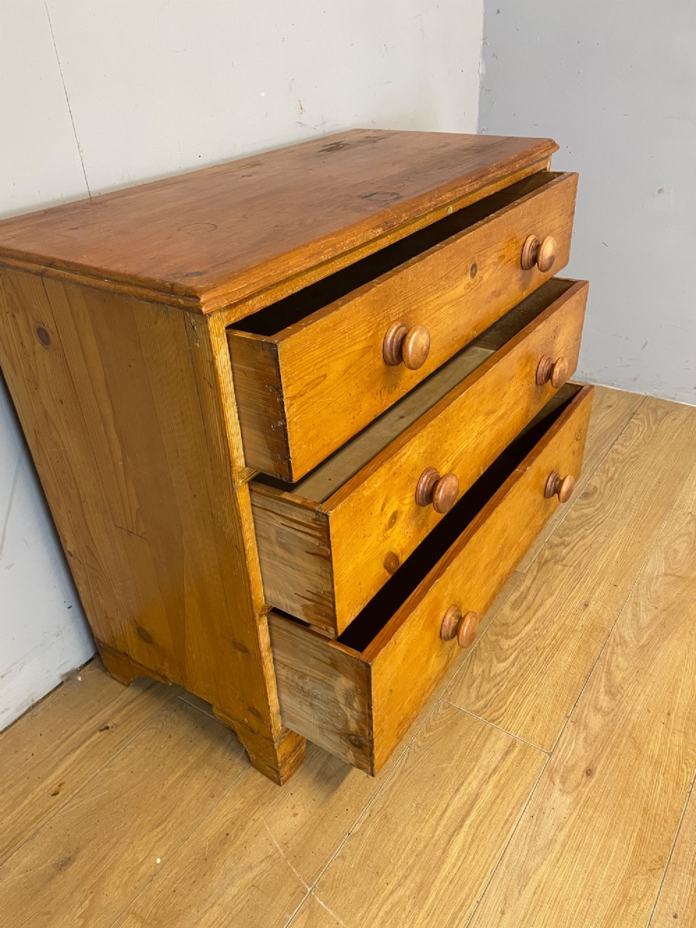 A nineteenth-century pine chest of drawers featuring three full-width drawers with turned wooden handles and bracket feet. View V