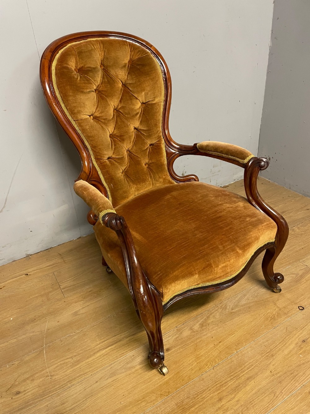 A Victorian walnut spoon back armchair featuring button-tufted mustard velvet upholstery, open carved armrests, and cabriole legs on brass castors. View II