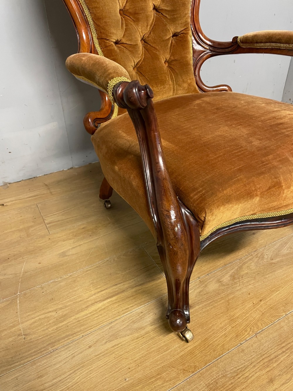 A Victorian walnut spoon back armchair featuring button-tufted mustard velvet upholstery, open carved armrests, and cabriole legs on brass castors. View III
