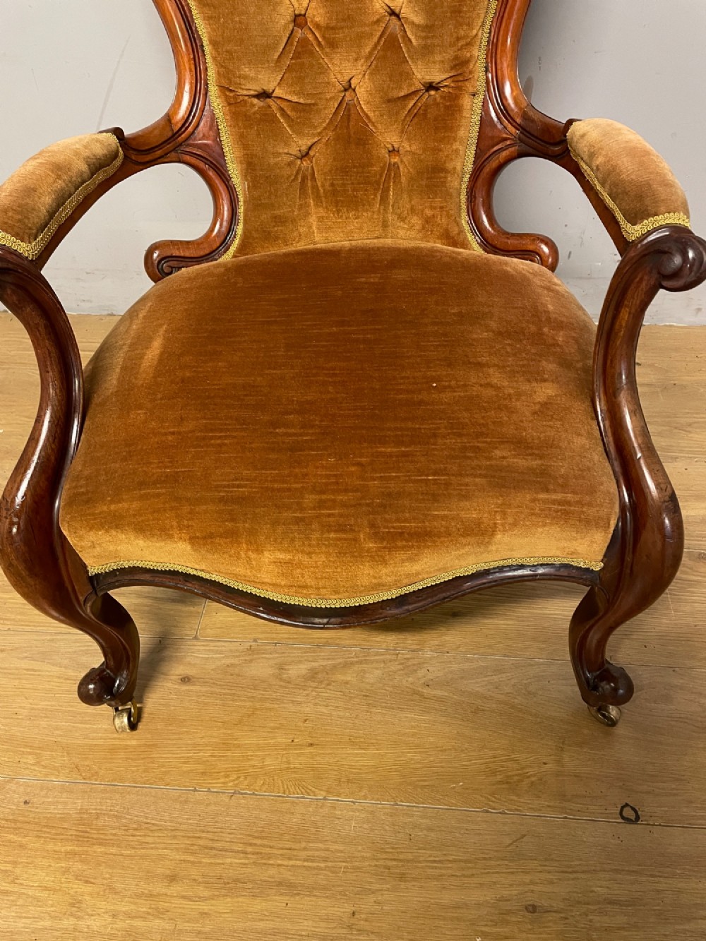 A Victorian walnut spoon back armchair featuring button-tufted mustard velvet upholstery, open carved armrests, and cabriole legs on brass castors. View V