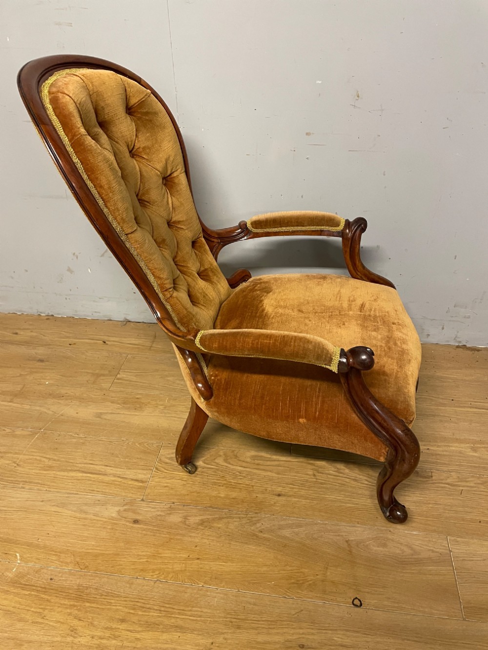 A Victorian walnut spoon back armchair featuring button-tufted mustard velvet upholstery, open carved armrests, and cabriole legs on brass castors. View VII