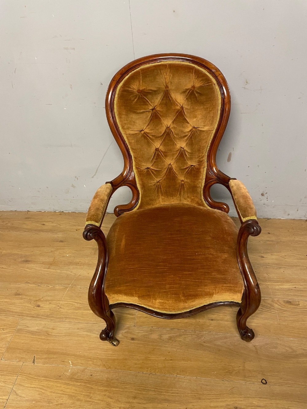 A Victorian walnut spoon back armchair featuring button-tufted mustard velvet upholstery, open carved armrests, and cabriole legs on brass castors. View XI