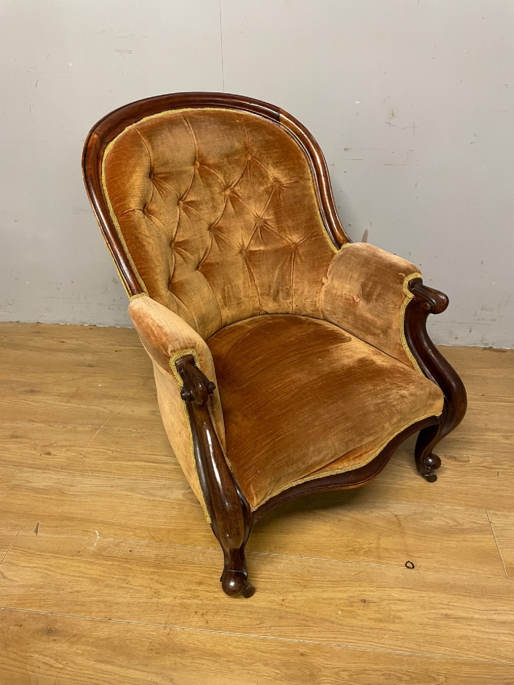 Victorian mahogany tub armchair upholstered in button-tufted amber velvet with curved front legs on brass castors. View X