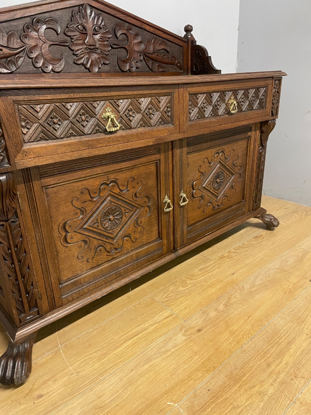 A nineteenth-century carved oak sideboard featuring a backboard gallery decorated with a Green Man motif, two geometric drawers, and two panelled cupboard doors. View IV