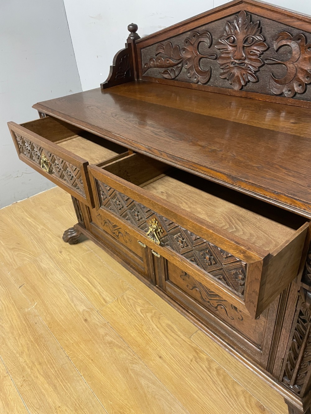 A nineteenth-century carved oak sideboard featuring a backboard gallery decorated with a Green Man motif, two geometric drawers, and two panelled cupboard doors. View VI