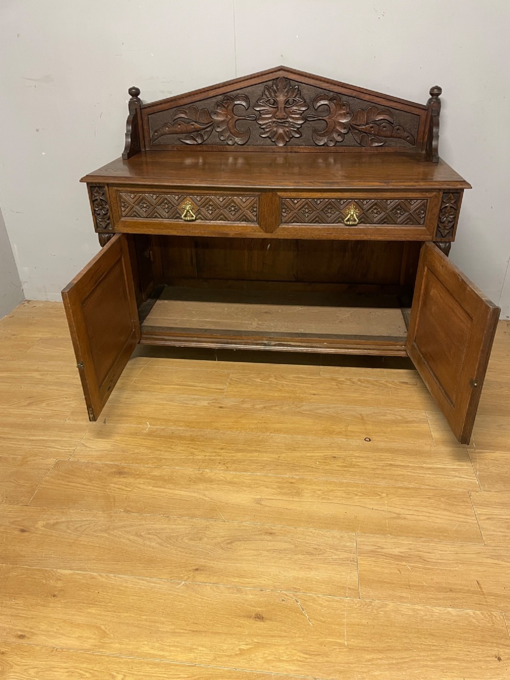 A nineteenth-century carved oak sideboard featuring a backboard gallery decorated with a Green Man motif, two geometric drawers, and two panelled cupboard doors. View VII