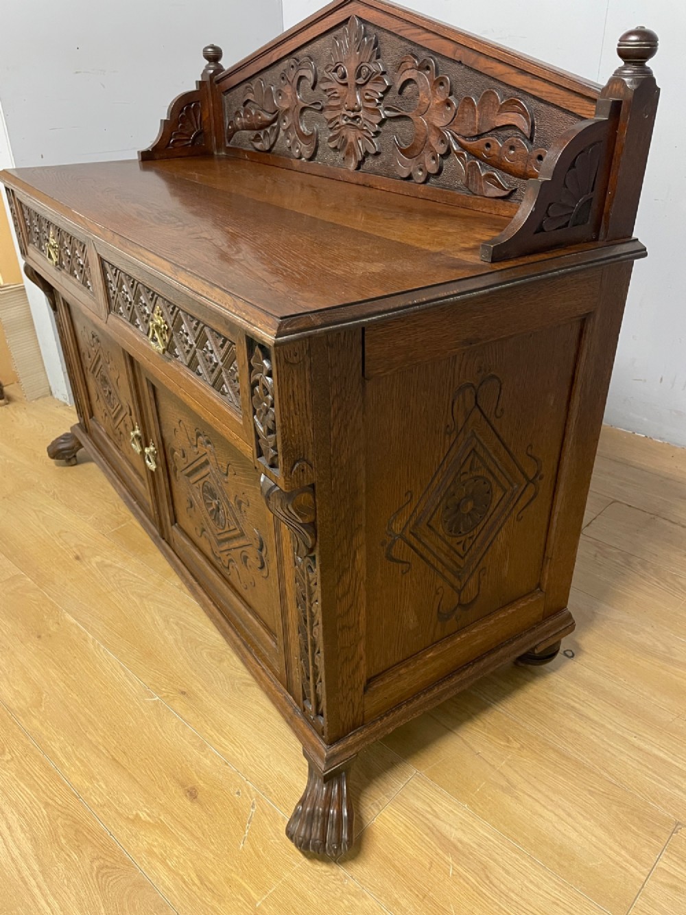 A nineteenth-century carved oak sideboard featuring a backboard gallery decorated with a Green Man motif, two geometric drawers, and two panelled cupboard doors. View IX