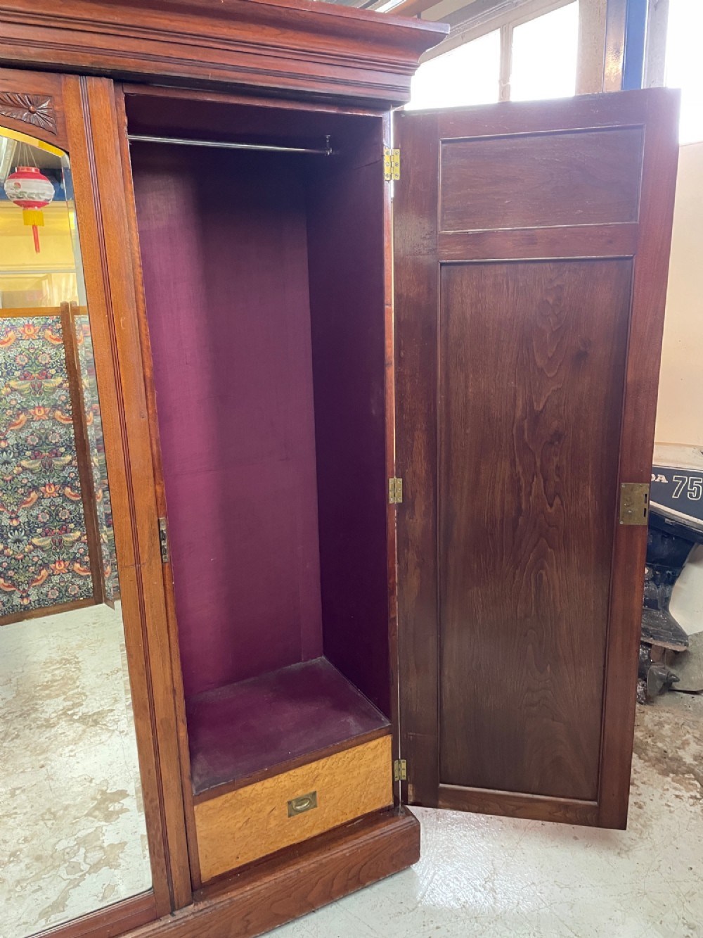 An Arts and Crafts walnut triple wardrobe featuring two outer timber doors with carved stylised flower panels and a central arched mirrored door with decorative brass hinges. View IX