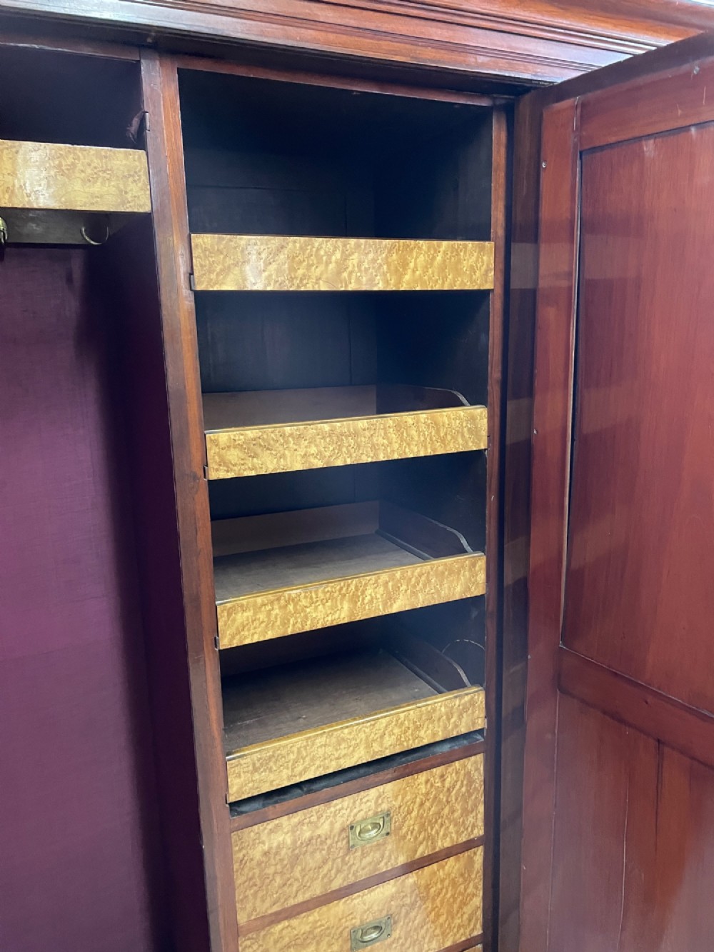 An Arts and Crafts walnut triple wardrobe featuring two outer timber doors with carved stylised flower panels and a central arched mirrored door with decorative brass hinges. View X