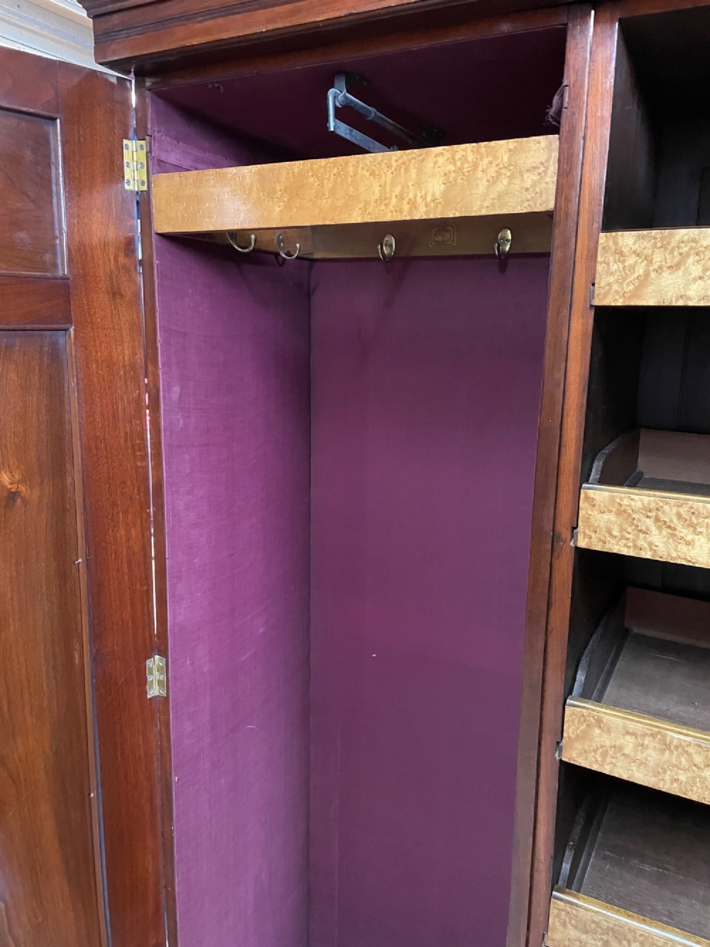 An Arts and Crafts walnut triple wardrobe featuring two outer timber doors with carved stylised flower panels and a central arched mirrored door with decorative brass hinges. View XII
