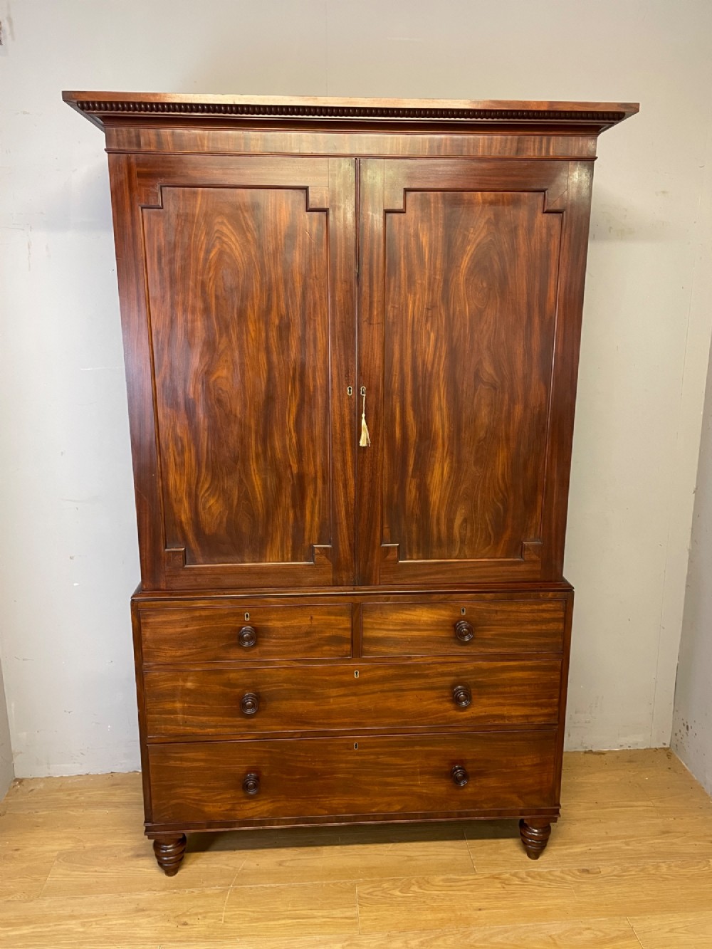 A two-part Regency flame mahogany linen press with twin panelled doors over four drawers with turned knobs. View II