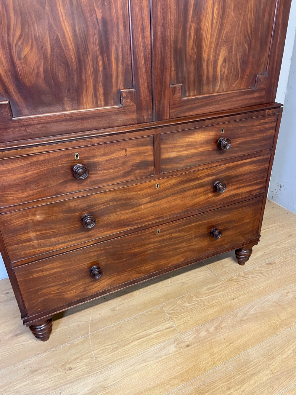 A two-part Regency flame mahogany linen press with twin panelled doors over four drawers with turned knobs. View III