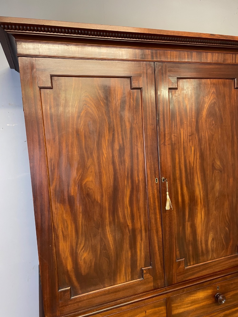 A two-part Regency flame mahogany linen press with twin panelled doors over four drawers with turned knobs. View IV