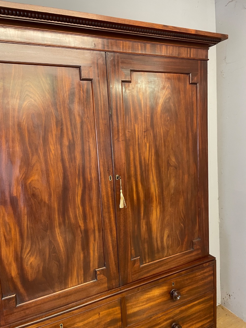 A two-part Regency flame mahogany linen press with twin panelled doors over four drawers with turned knobs. View V