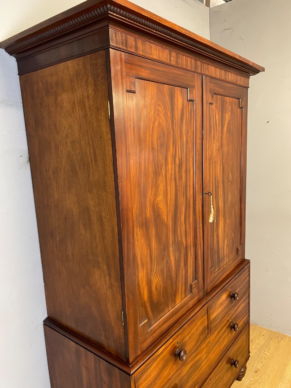 A two-part Regency flame mahogany linen press with twin panelled doors over four drawers with turned knobs. View VII