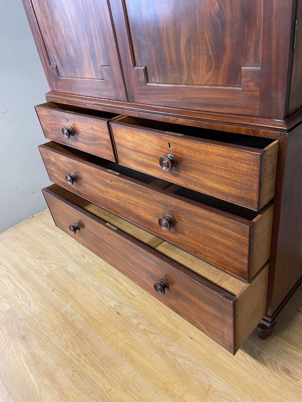 A two-part Regency flame mahogany linen press with twin panelled doors over four drawers with turned knobs. View IX
