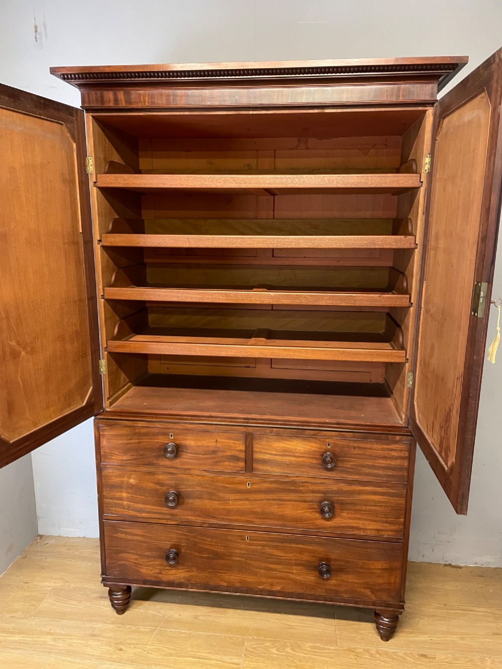 A two-part Regency flame mahogany linen press with twin panelled doors over four drawers with turned knobs. View X