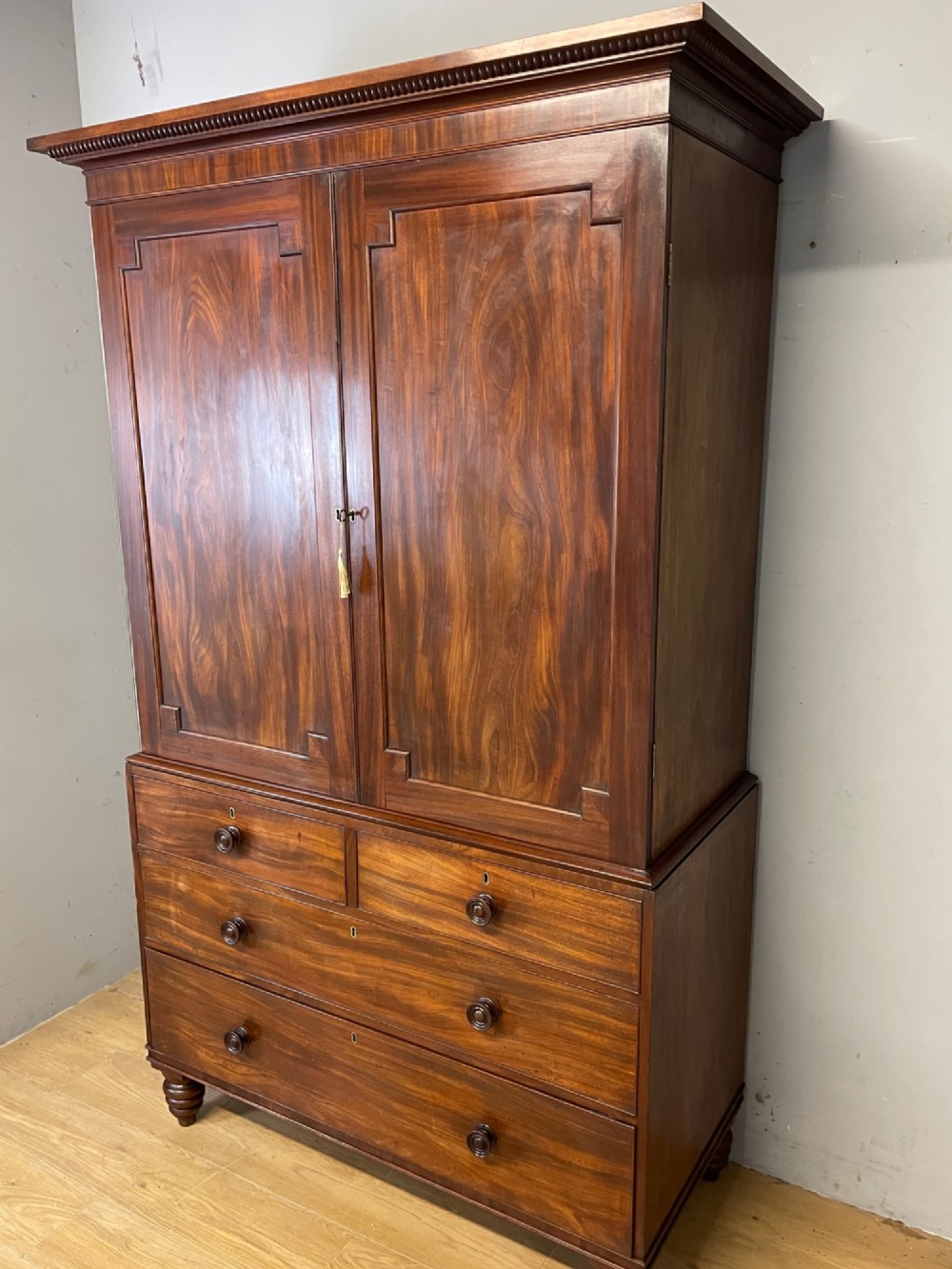 A two-part Regency flame mahogany linen press with twin panelled doors over four drawers with turned knobs. View XI