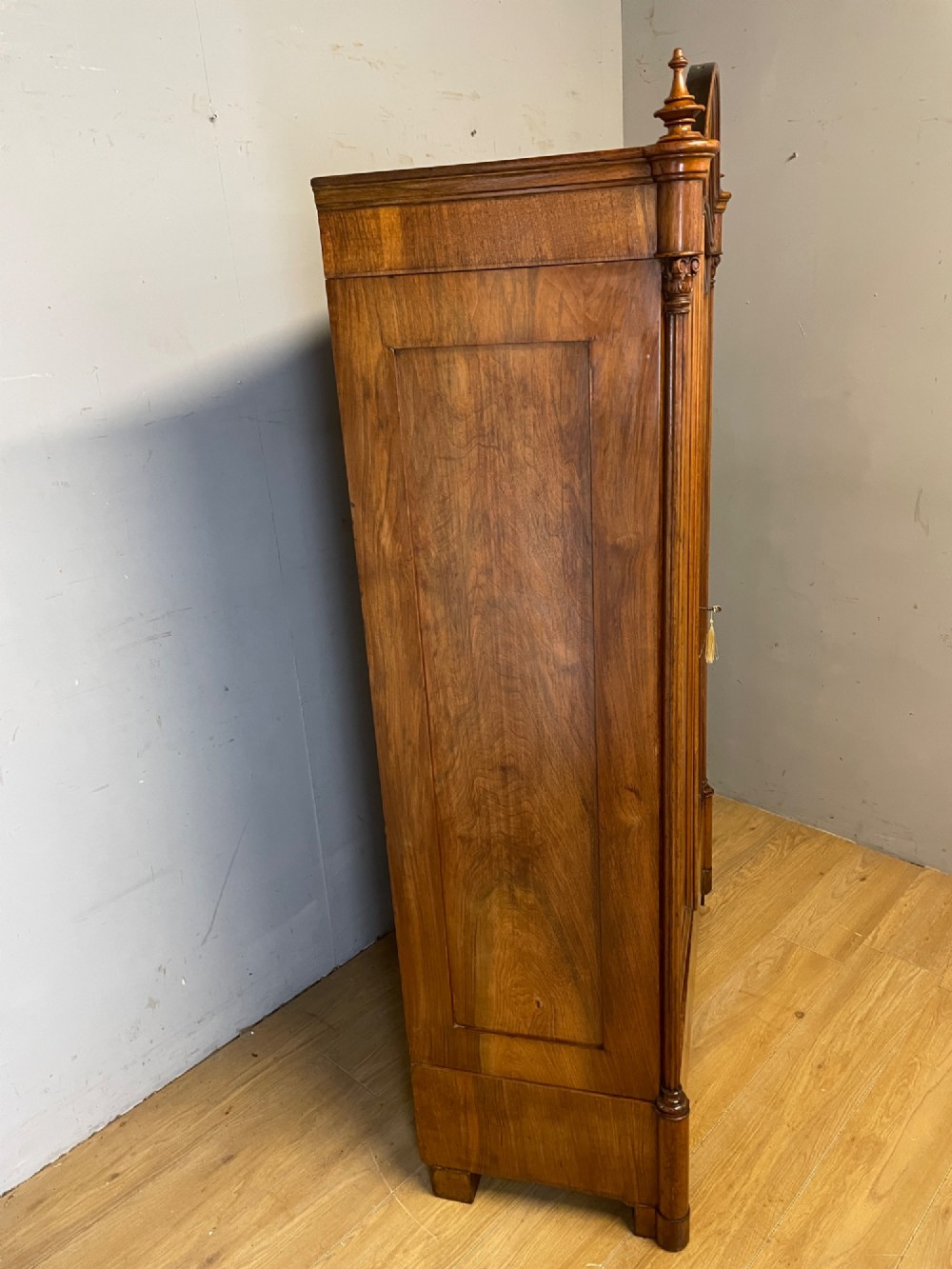 A nineteenth-century French figured walnut two-door armoire featuring an arched cornice with turned corner finials and a central circular moulding. View IX
