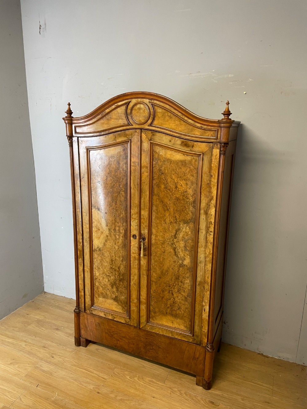 A nineteenth-century French figured walnut two-door armoire featuring an arched cornice with turned corner finials and a central circular moulding. View XII
