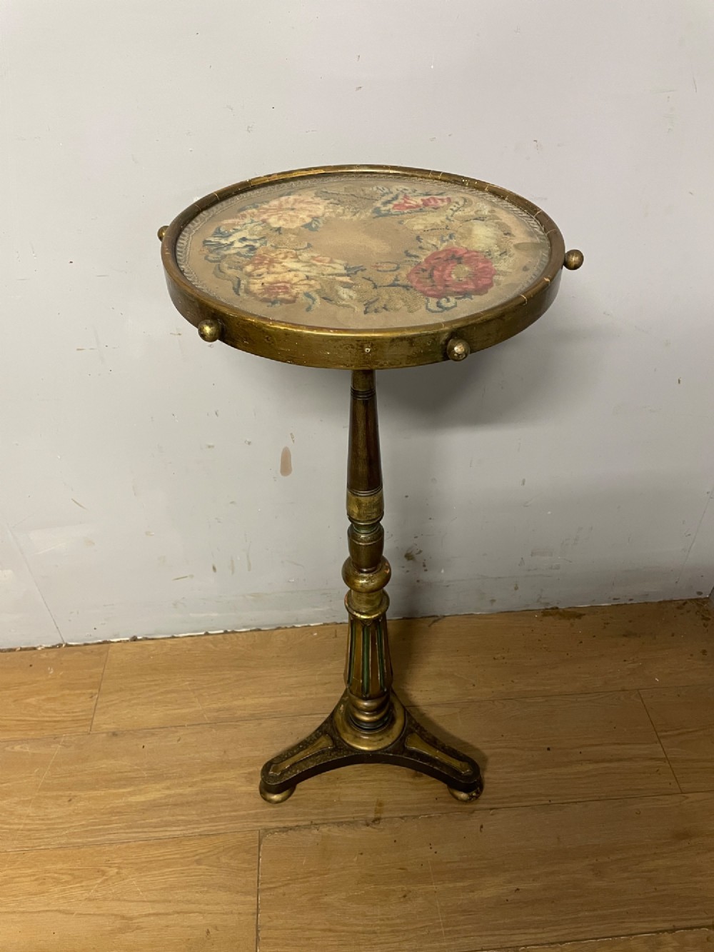 A 19th-century gilt and ebonised torchere stand featuring a circular needlework top, a turned column stem, and tripod feet.