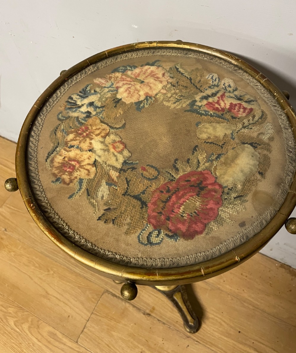 A 19th-century gilt and ebonised torchere stand featuring a circular needlework top, a turned column stem, and tripod feet. View V