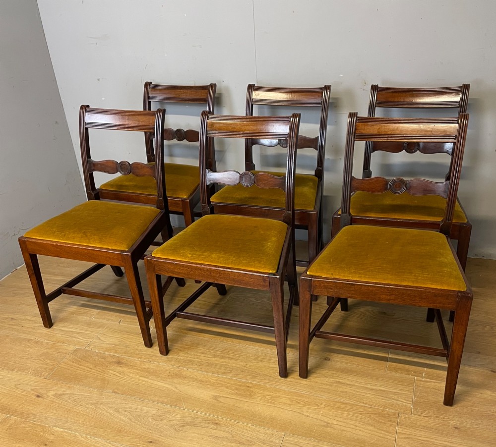 A set of six Georgian mahogany dining chairs featuring reeded frames, carved back rails with roundels, square legs with stretchers, and gold velvet seats.