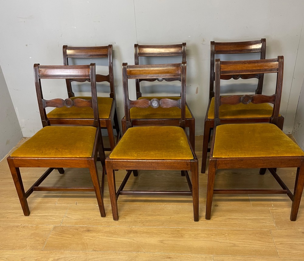 A set of six Georgian mahogany dining chairs featuring reeded frames, carved back rails with roundels, square legs with stretchers, and gold velvet seats. View II
