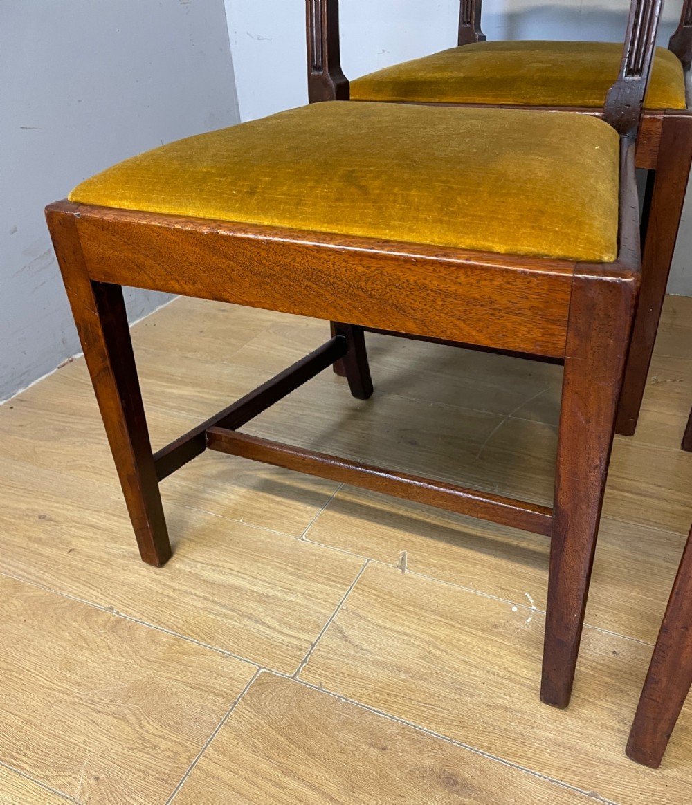 A set of six Georgian mahogany dining chairs featuring reeded frames, carved back rails with roundels, square legs with stretchers, and gold velvet seats. View IV