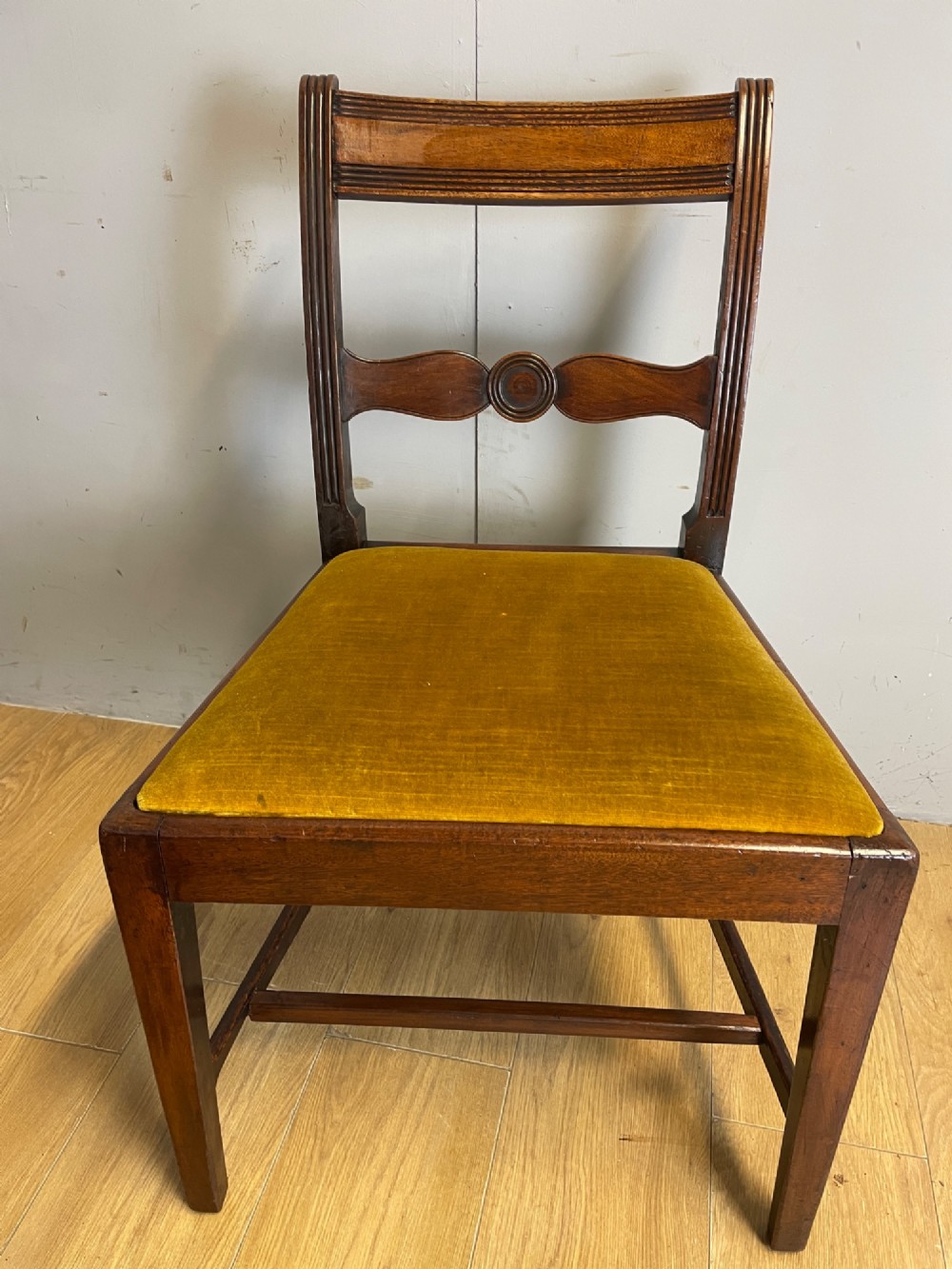 A set of six Georgian mahogany dining chairs featuring reeded frames, carved back rails with roundels, square legs with stretchers, and gold velvet seats. View V