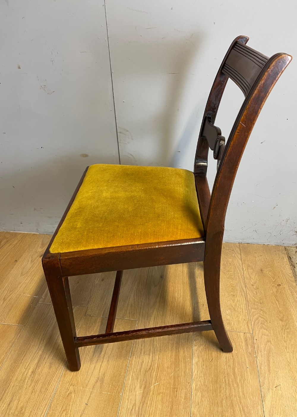 A set of six Georgian mahogany dining chairs featuring reeded frames, carved back rails with roundels, square legs with stretchers, and gold velvet seats. View VI