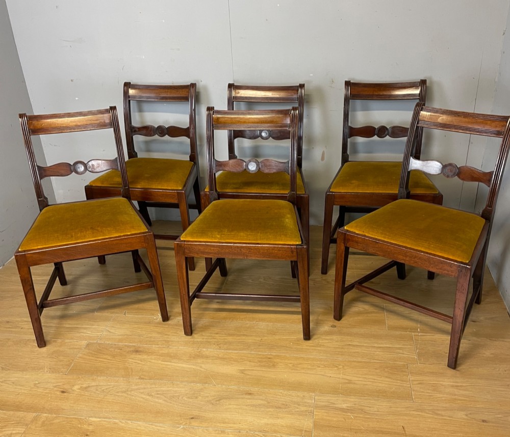 A set of six Georgian mahogany dining chairs featuring reeded frames, carved back rails with roundels, square legs with stretchers, and gold velvet seats. View XI