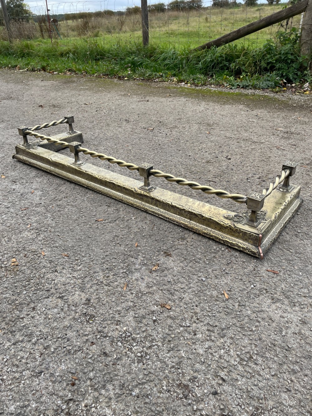 A 19th-century brass fireplace fender featuring a twisted top rail supported by four square columns over an embossed base.