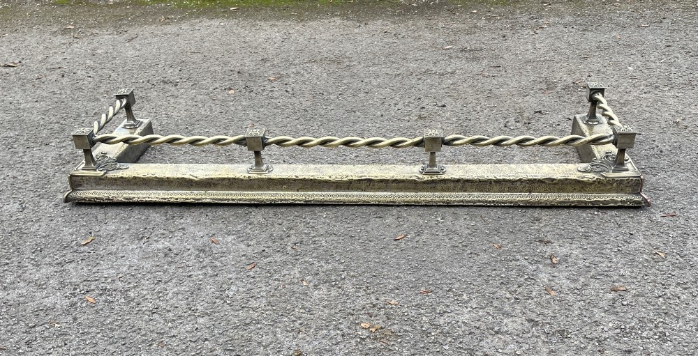 A 19th-century brass fireplace fender featuring a twisted top rail supported by four square columns over an embossed base. View II