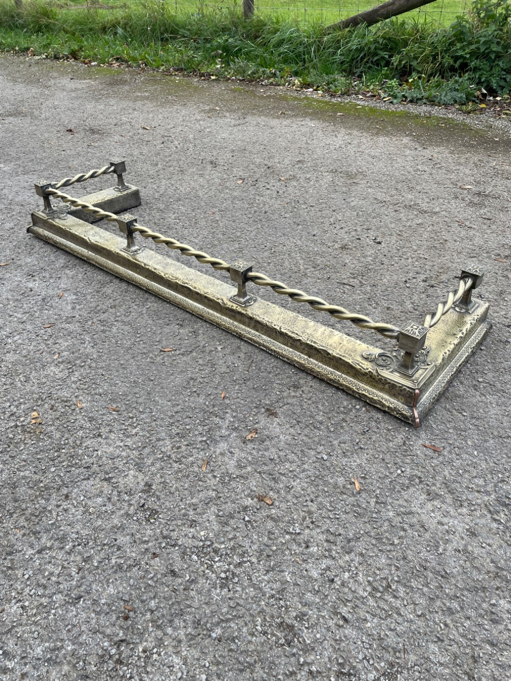 A 19th-century brass fireplace fender featuring a twisted top rail supported by four square columns over an embossed base. View III