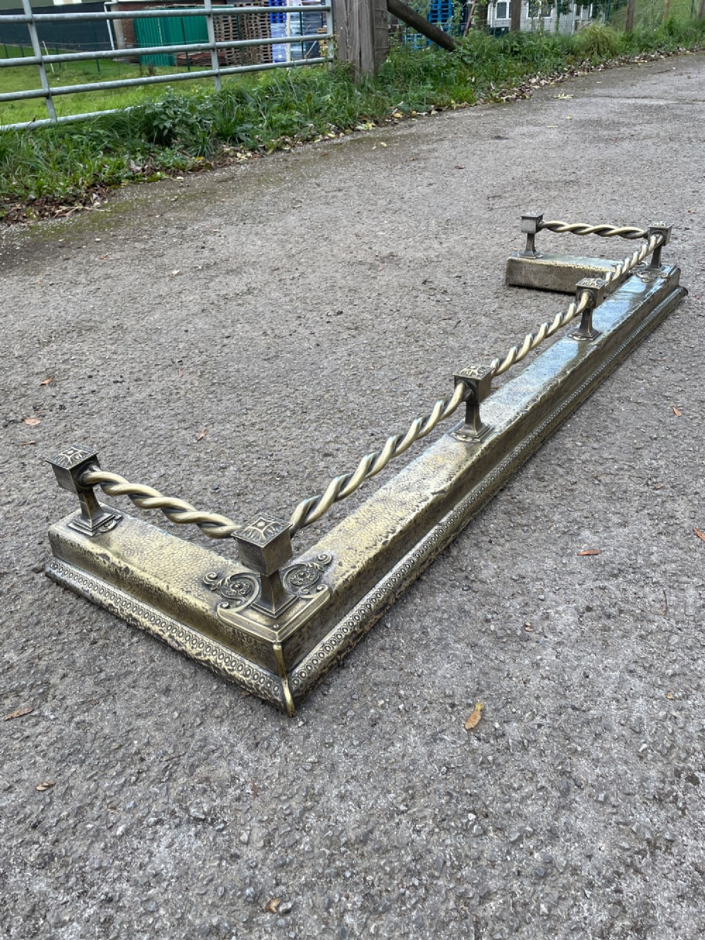 A 19th-century brass fireplace fender featuring a twisted top rail supported by four square columns over an embossed base. View V
