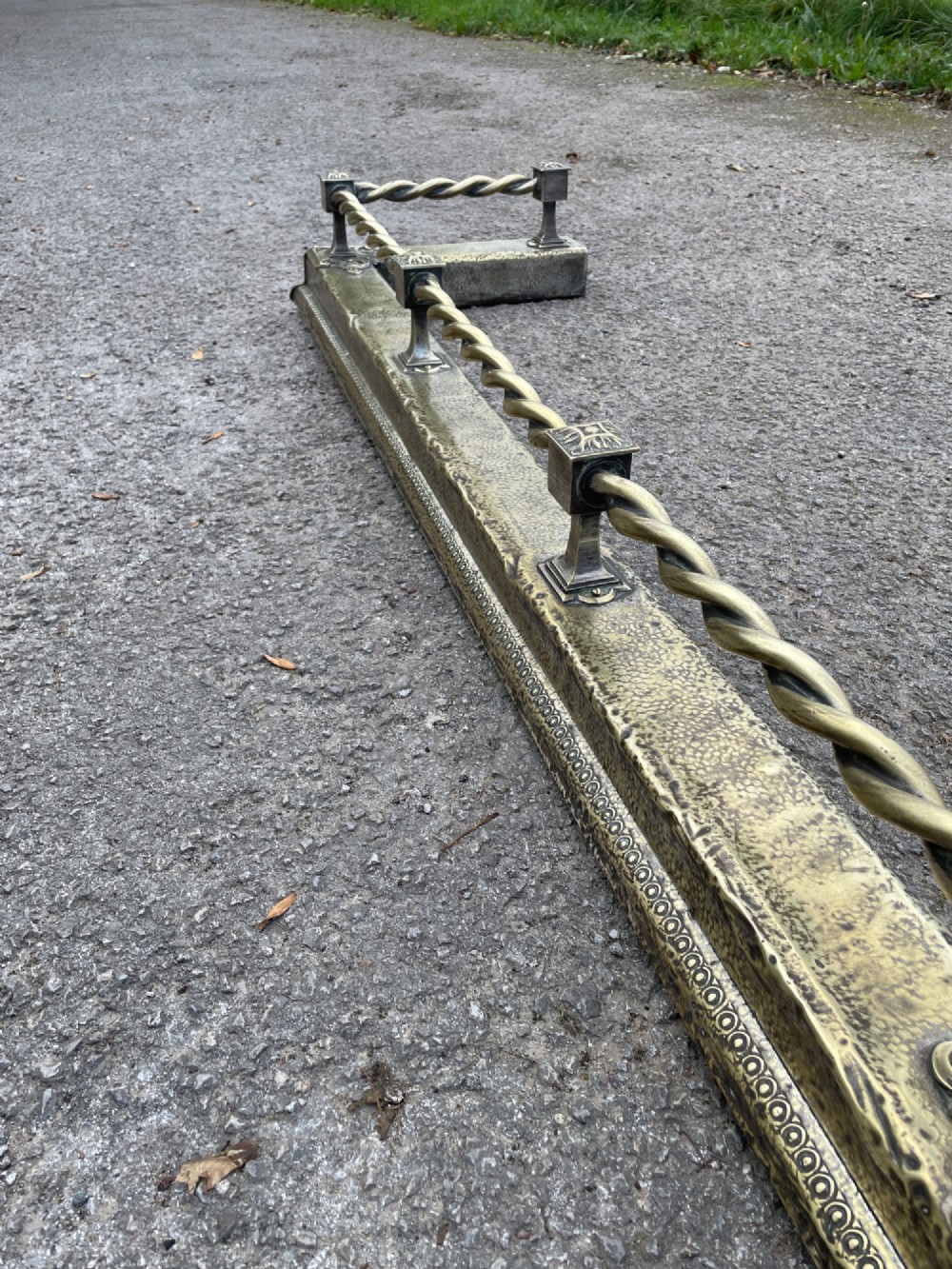 A 19th-century brass fireplace fender featuring a twisted top rail supported by four square columns over an embossed base. View VII