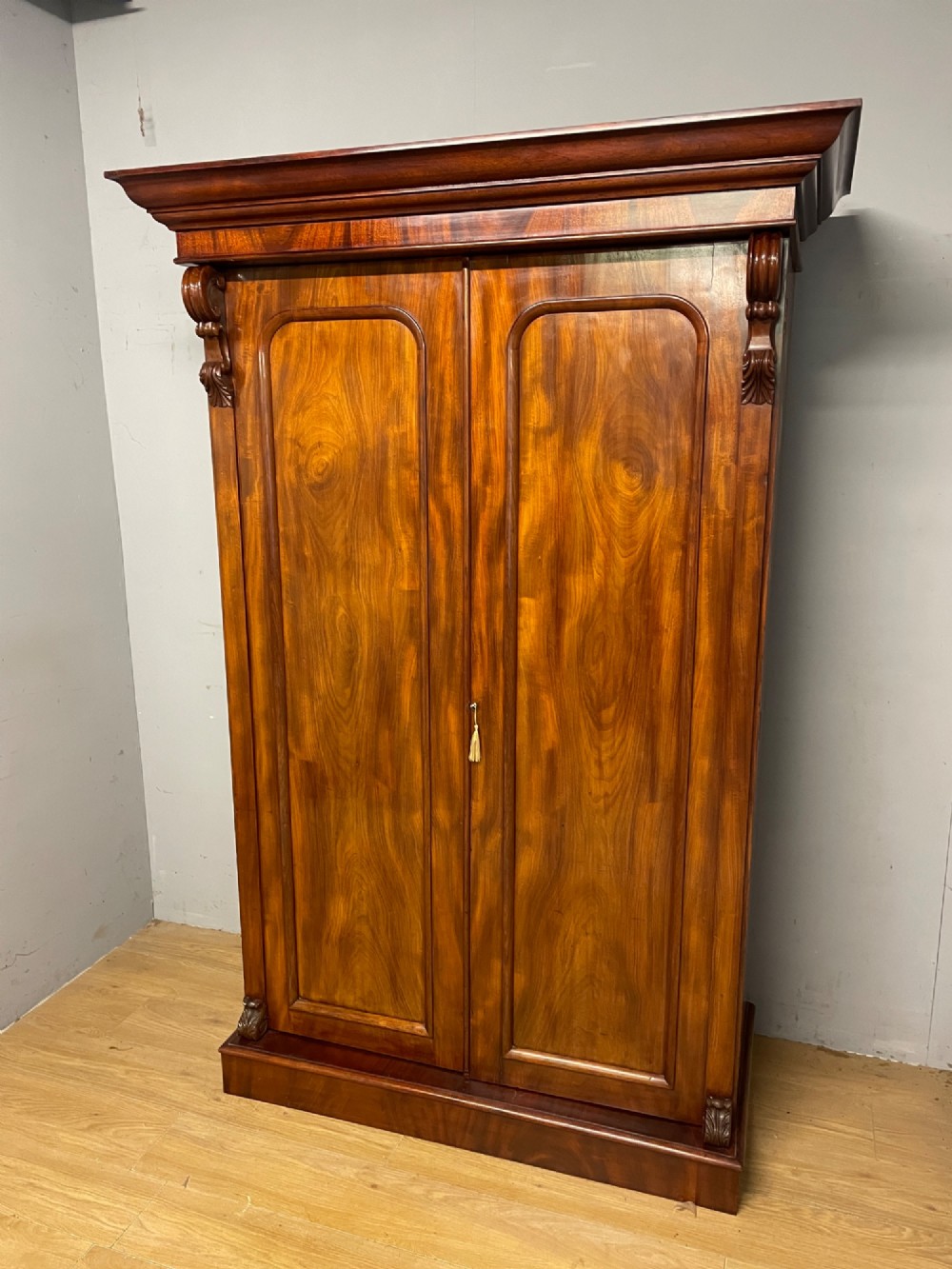 A 19th-century double wardrobe constructed from flame mahogany featuring two arched panelled doors, carved corbel accents, a moulded cornice, and a flat plinth base. View II