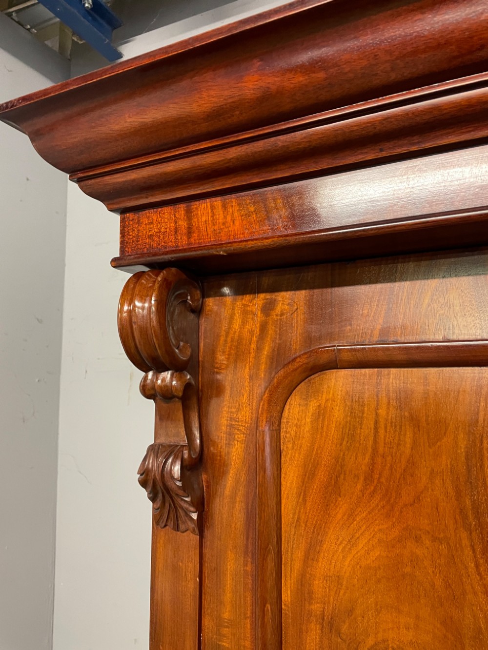 A 19th-century double wardrobe constructed from flame mahogany featuring two arched panelled doors, carved corbel accents, a moulded cornice, and a flat plinth base. View V