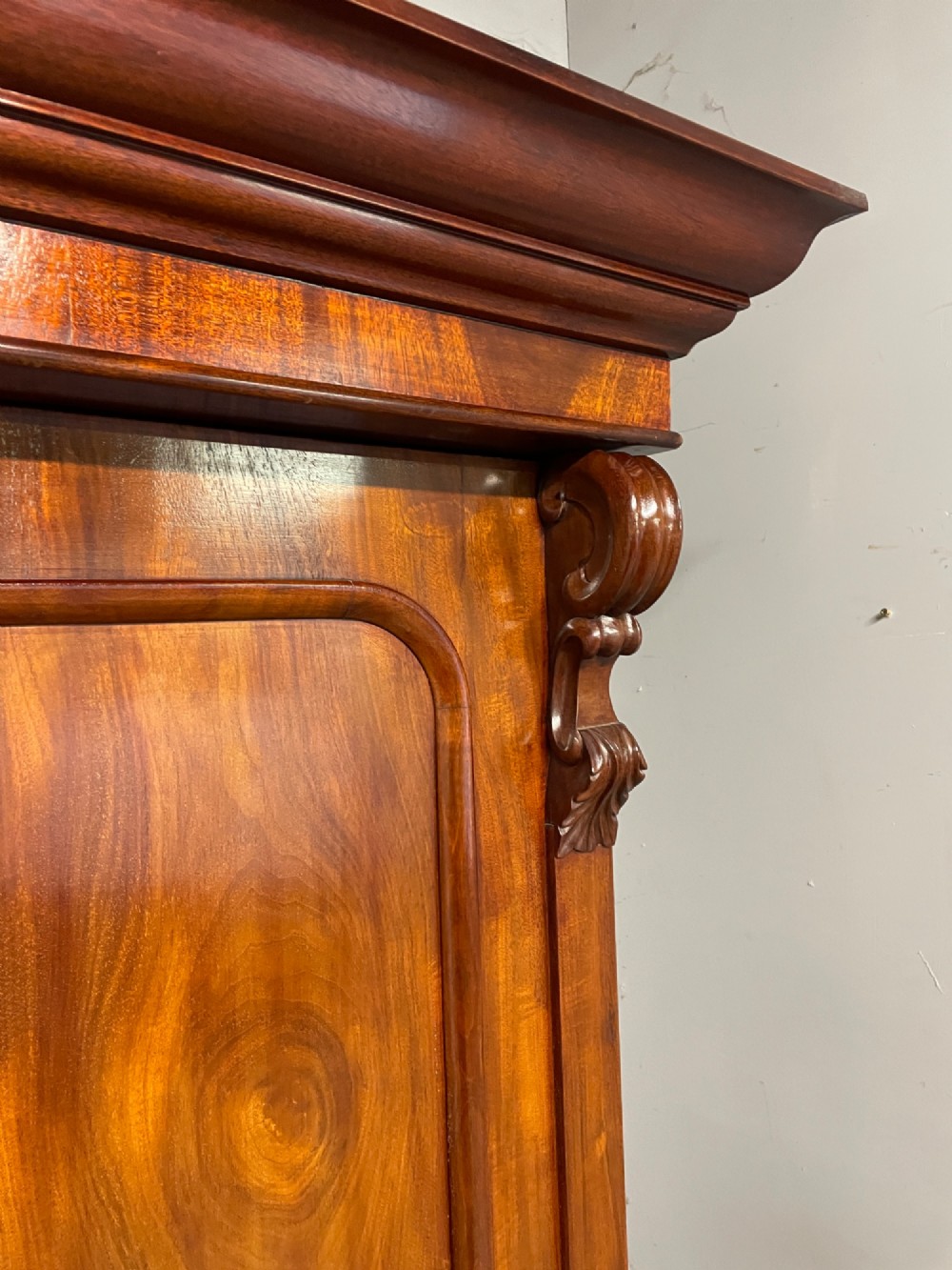 A 19th-century double wardrobe constructed from flame mahogany featuring two arched panelled doors, carved corbel accents, a moulded cornice, and a flat plinth base. View VI