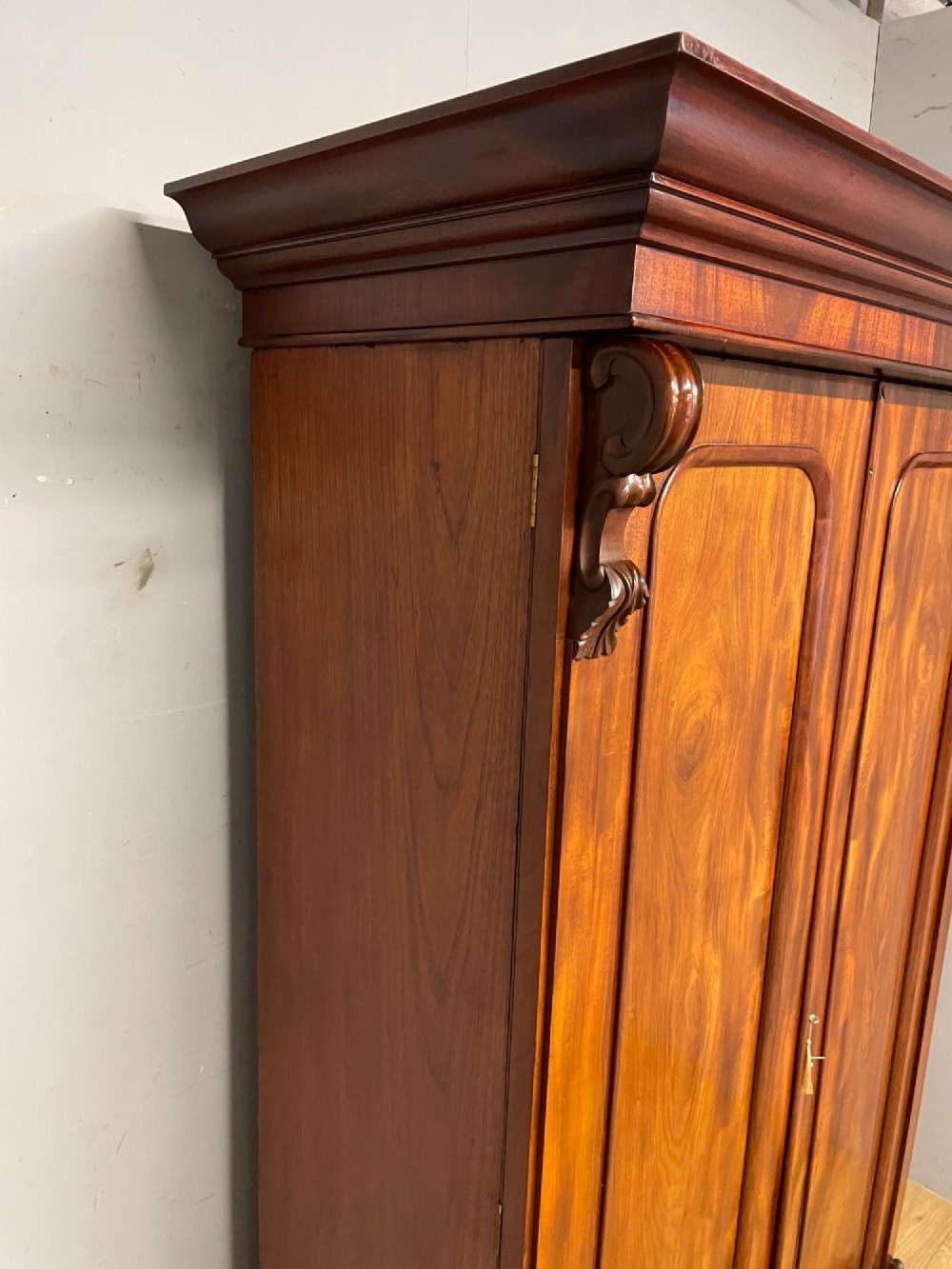 A 19th-century double wardrobe constructed from flame mahogany featuring two arched panelled doors, carved corbel accents, a moulded cornice, and a flat plinth base. View X