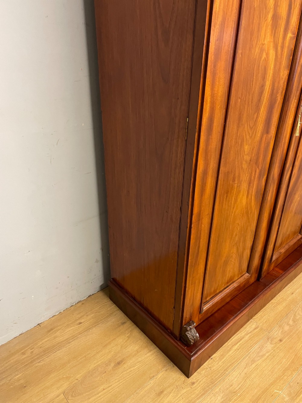 A 19th-century double wardrobe constructed from flame mahogany featuring two arched panelled doors, carved corbel accents, a moulded cornice, and a flat plinth base. View XI
