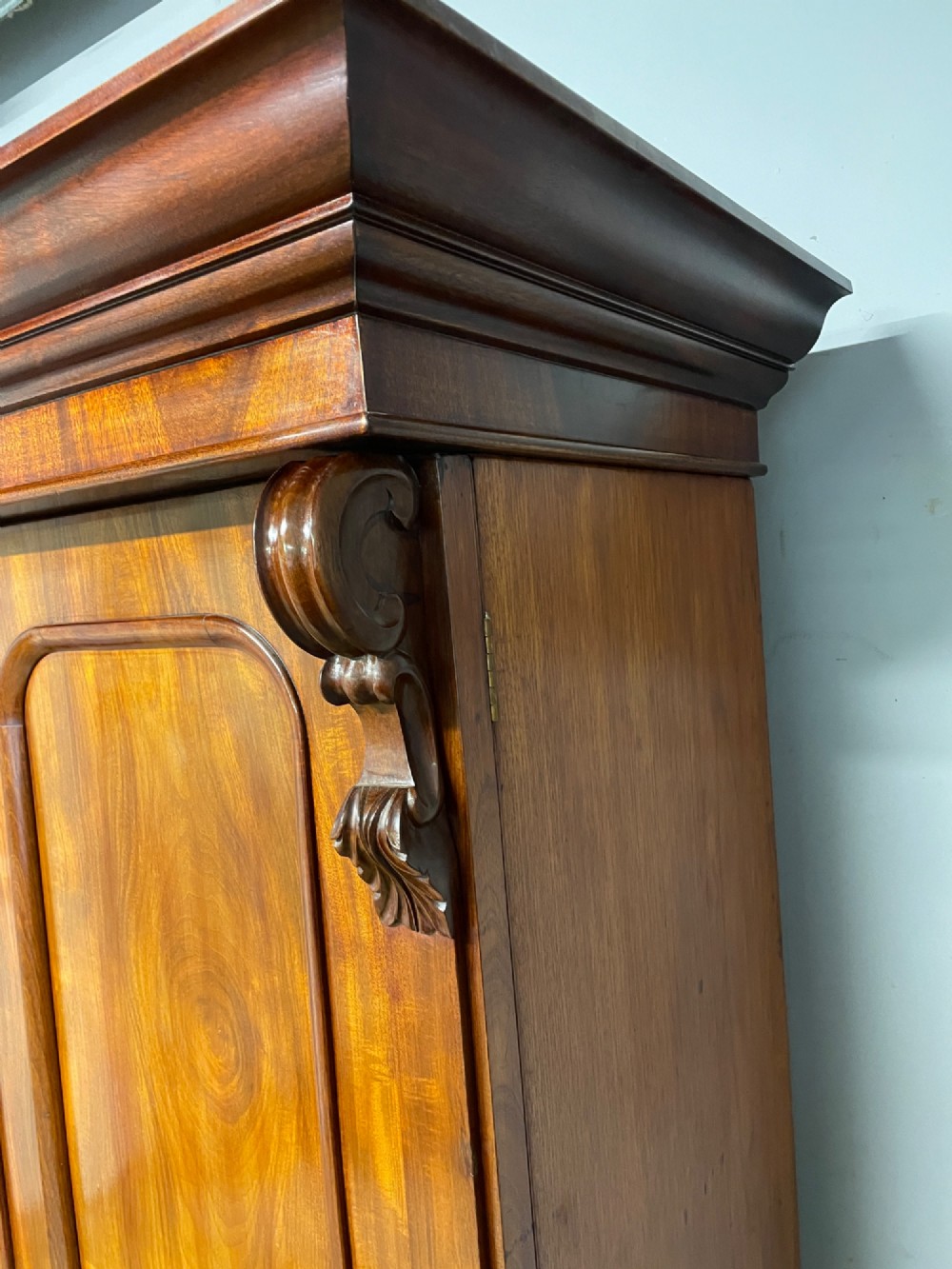 A 19th-century double wardrobe constructed from flame mahogany featuring two arched panelled doors, carved corbel accents, a moulded cornice, and a flat plinth base. View XII