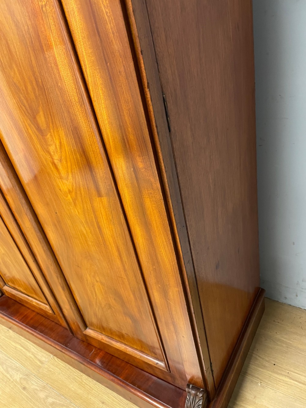 A 19th-century double wardrobe constructed from flame mahogany featuring two arched panelled doors, carved corbel accents, a moulded cornice, and a flat plinth base. View XIV