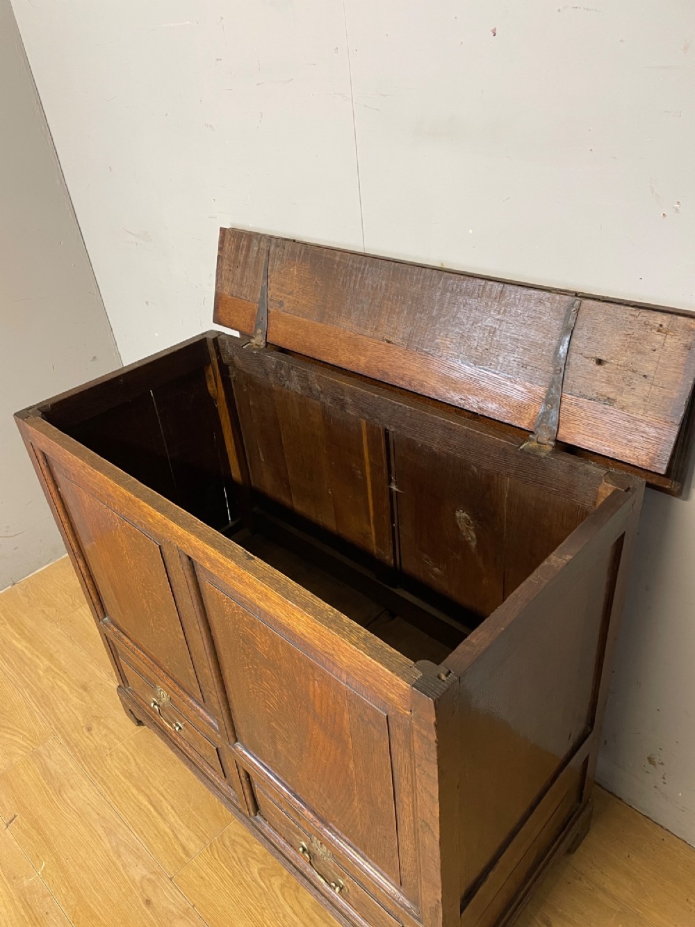A nineteenth-century dark oak mule chest featuring a hinged lid, two front raised field panels, and two lower drawers with brass swan-neck handles. View V