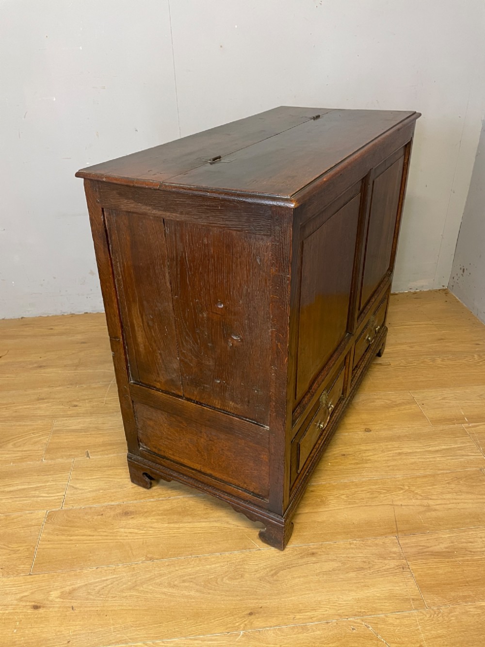 A nineteenth-century dark oak mule chest featuring a hinged lid, two front raised field panels, and two lower drawers with brass swan-neck handles. View VIII