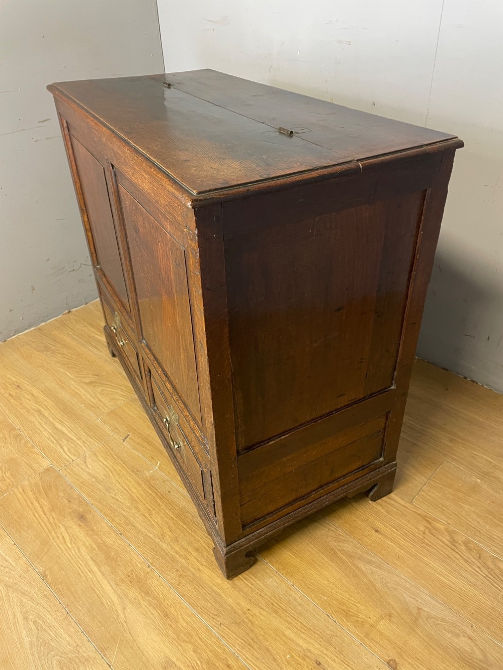 A nineteenth-century dark oak mule chest featuring a hinged lid, two front raised field panels, and two lower drawers with brass swan-neck handles. View IX