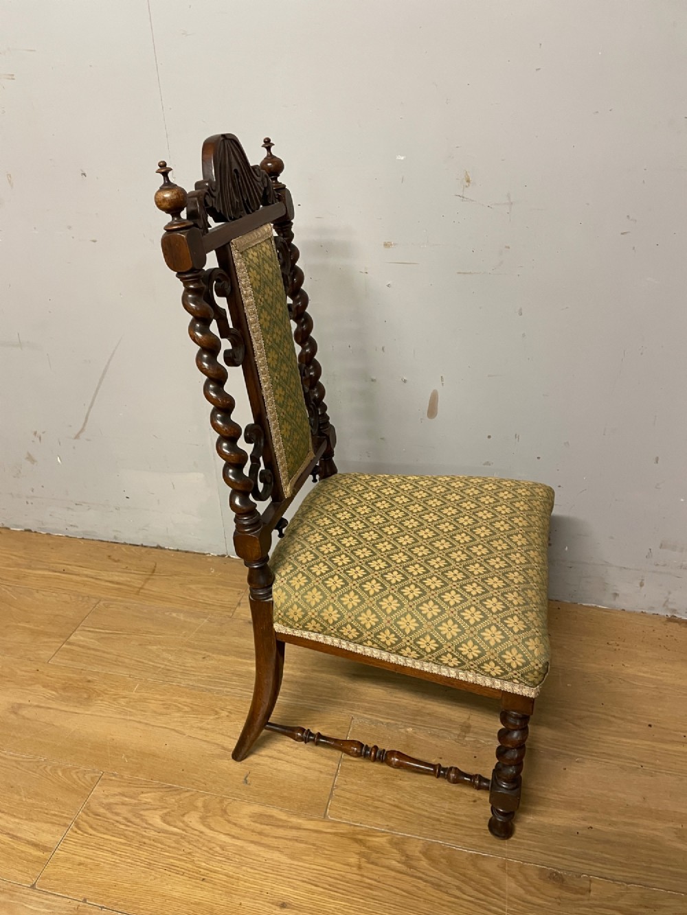 A nineteenth-century carved rosewood nursing chair featuring barley twist uprights, scrollwork cresting, and patterned green upholstery on the seat and back panel. View V