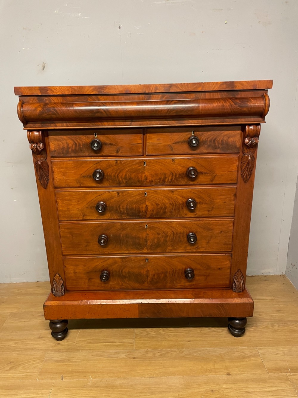 A 19th-century Scottish flame mahogany chest of drawers featuring a top cushion drawer, carved corbels, five lower drawers with turned wooden knobs, and turned feet. View II