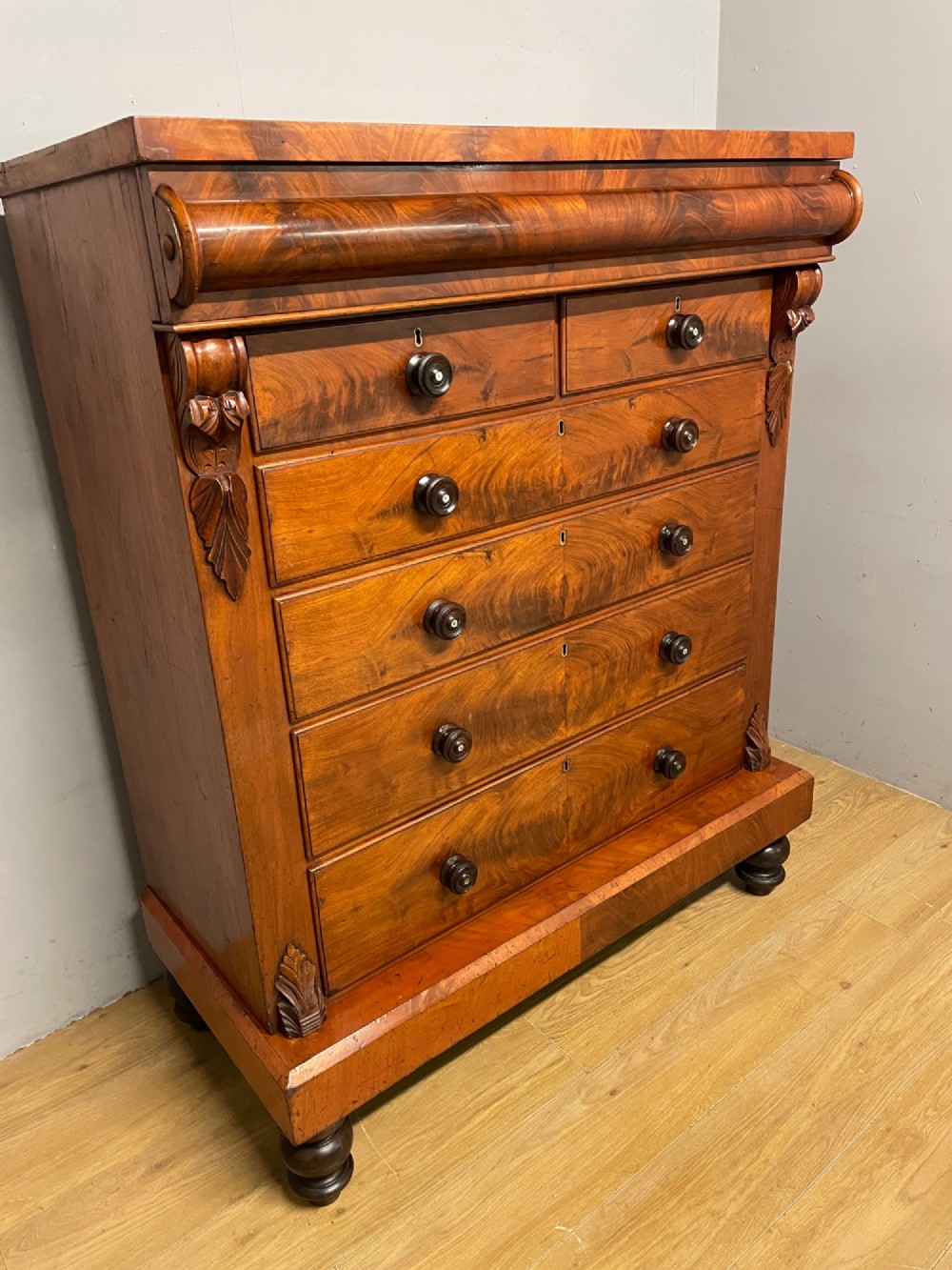 A 19th-century Scottish flame mahogany chest of drawers featuring a top cushion drawer, carved corbels, five lower drawers with turned wooden knobs, and turned feet. View III